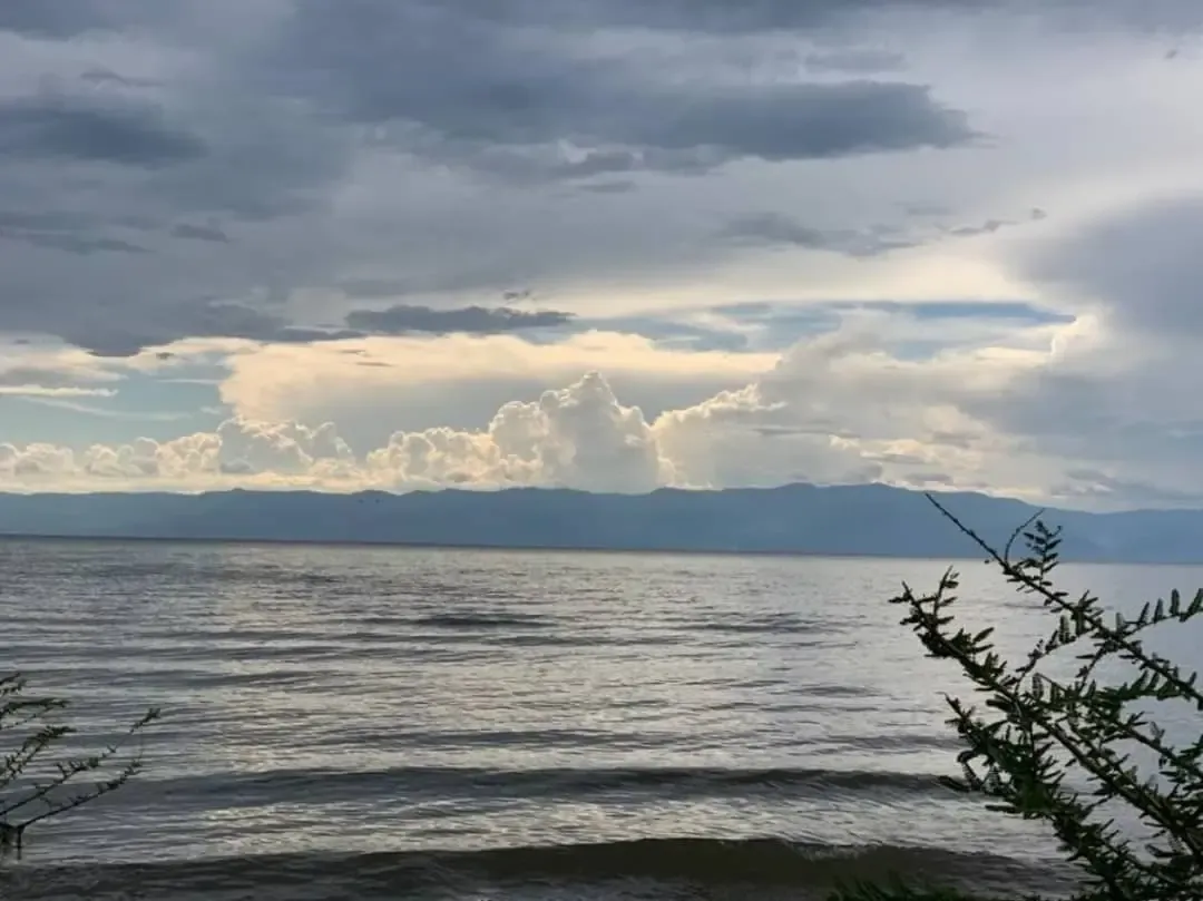 Open water under a bank of tall cloud, with a low ridge of hills along the far shore.